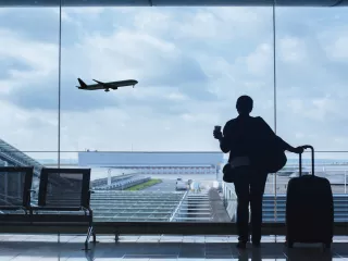 Woman with suitcase watching plane take off at airport