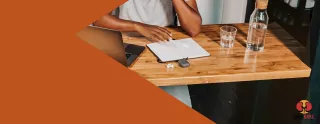 Image of a person seated at a table, looking at a laptop